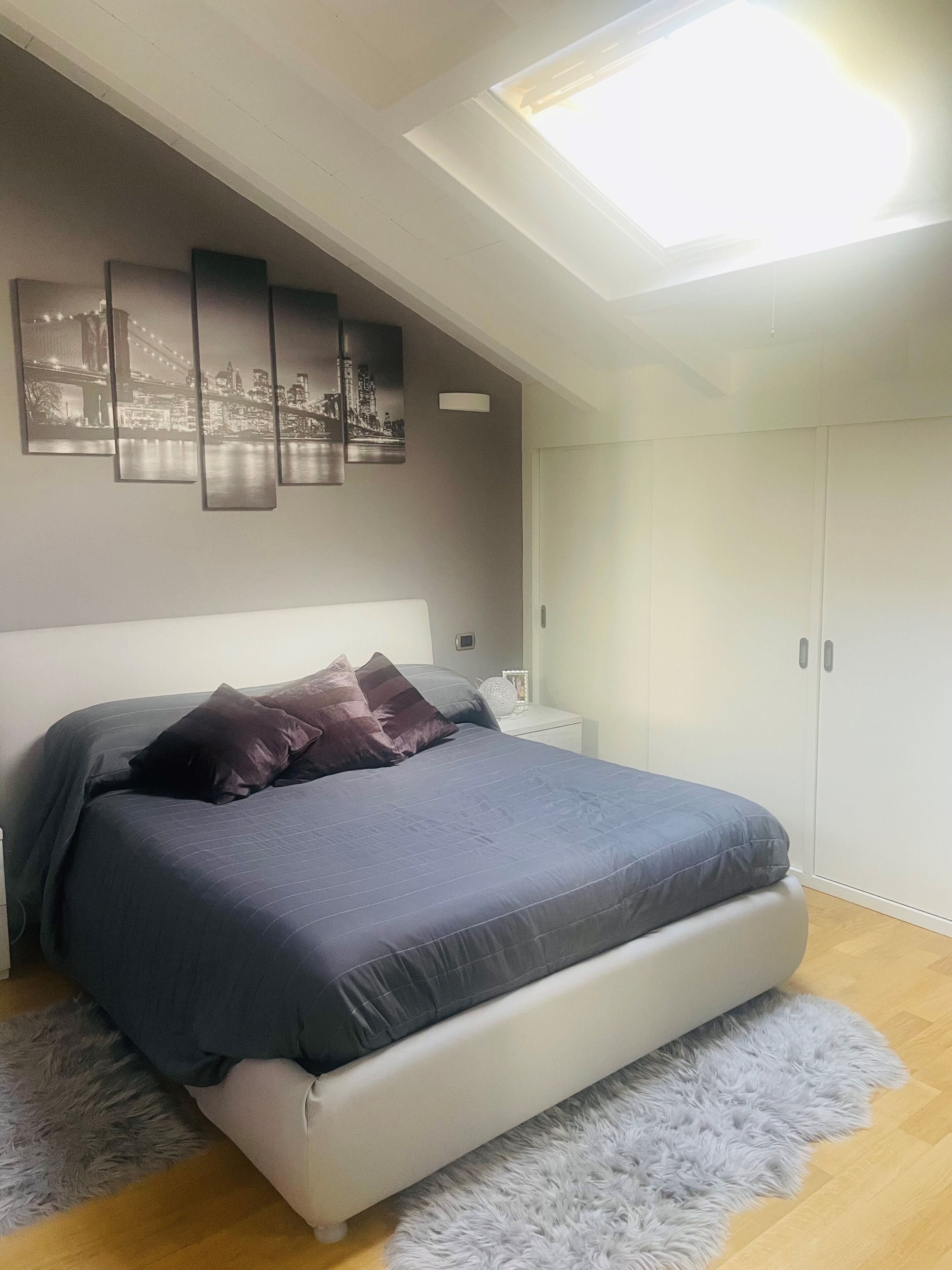 A bedroom with a bed, a nightstand, a wardrobe, and a skylight.