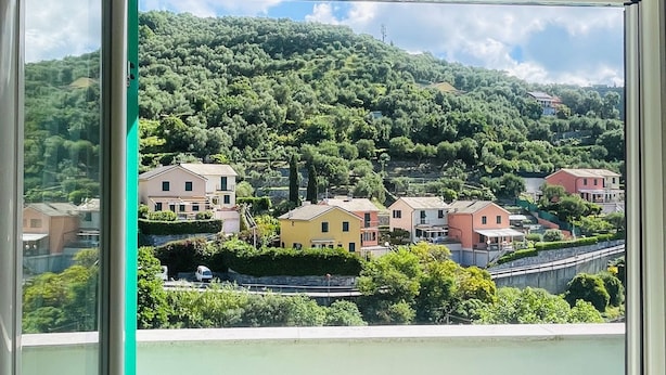 A balcony with a view of a hillside village, featuring residential buildings and lush greenery.