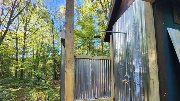 A rustic wooden cabin with a metal door, surrounded by a forest. - Bourbon St BlueBird Bus + HOT TUB on 10 ACRES (BItely)