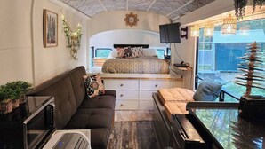 A compact, well-lit room with a bed, sofa, and a small dining area. - Bourbon St BlueBird Bus + HOT TUB on 10 ACRES (BItely)