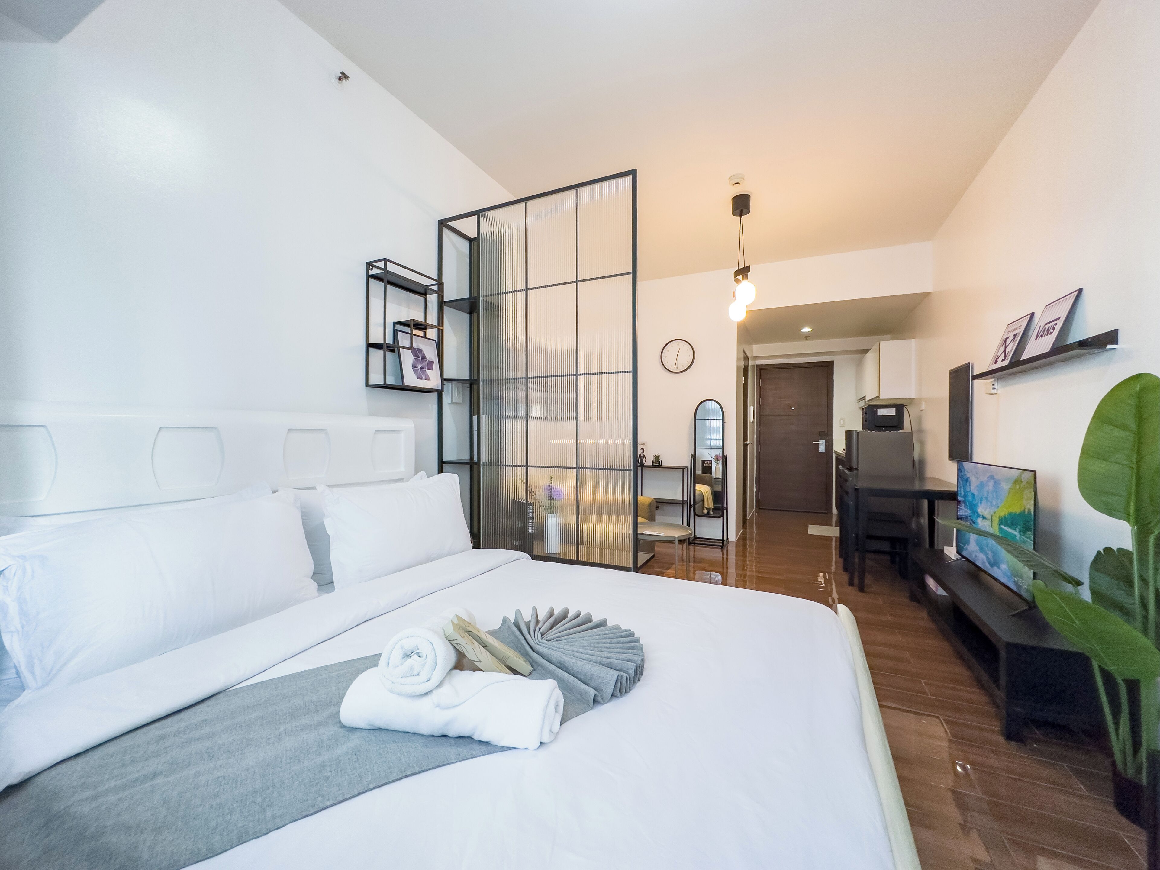 A modern hotel room with a large bed, a desk, a chair, a TV, and a plant.