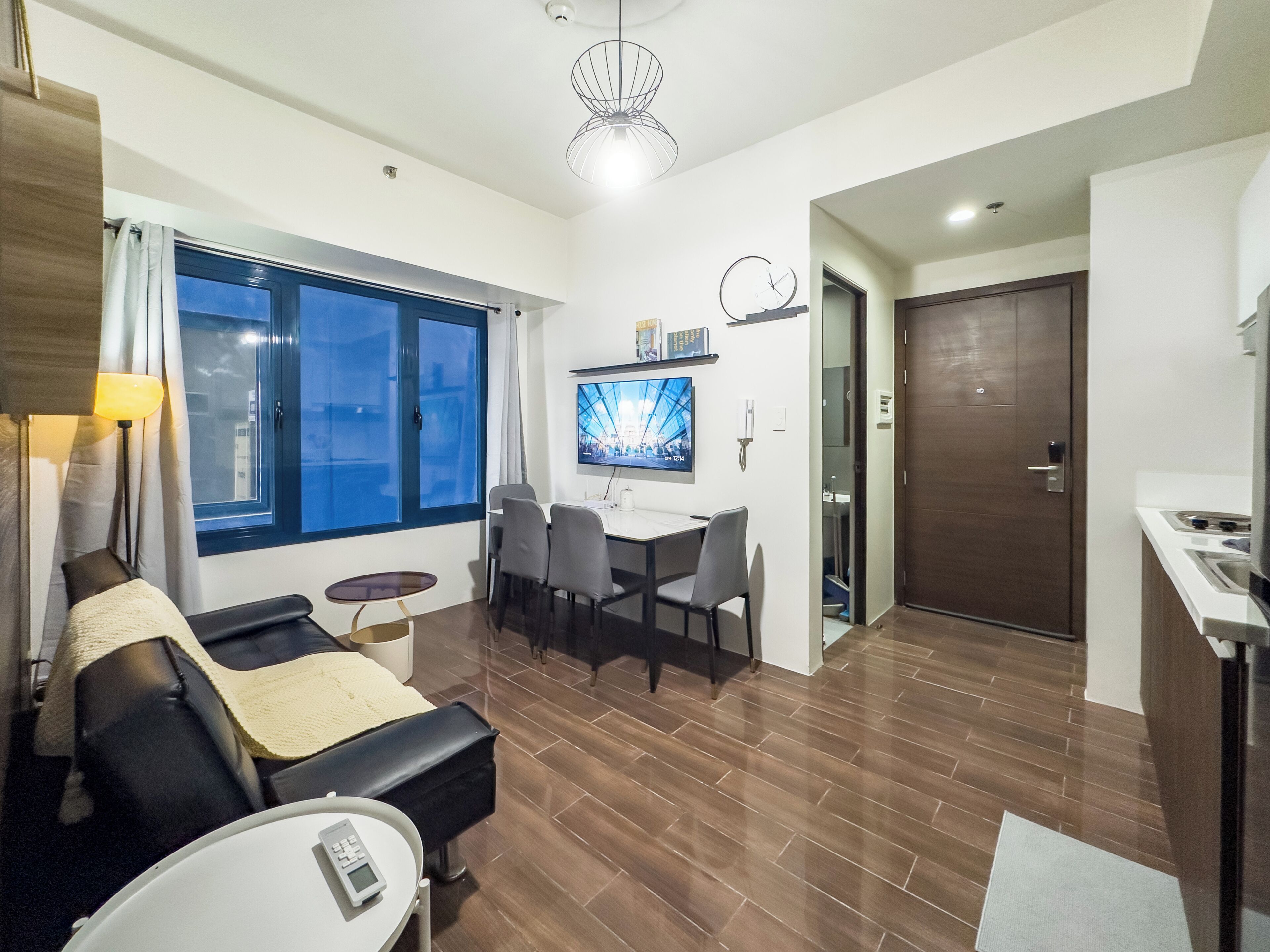 A modern living room with a sofa, a small table, a TV, and a dining area with chairs.