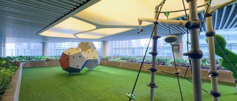 An indoor play area with artificial grass, climbing structures, and a large geometric sculpture.