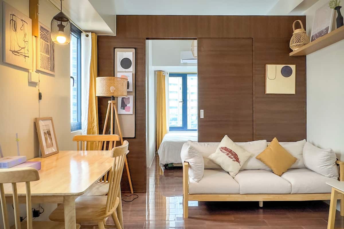 A modern living room with a wooden dining table, a sofa with cushions, and a wall-mounted shelf with decorative items.