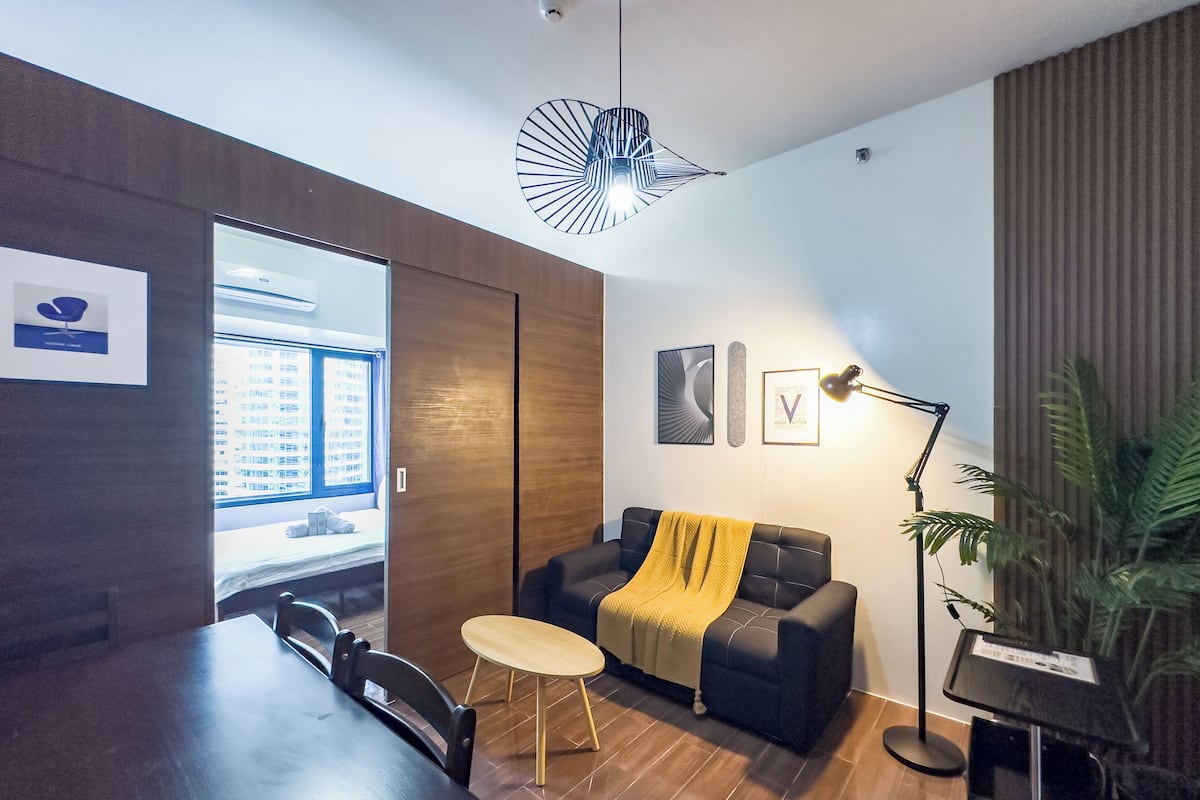 A modern living room with a sofa, a coffee table, a dining table, and a pendant light.