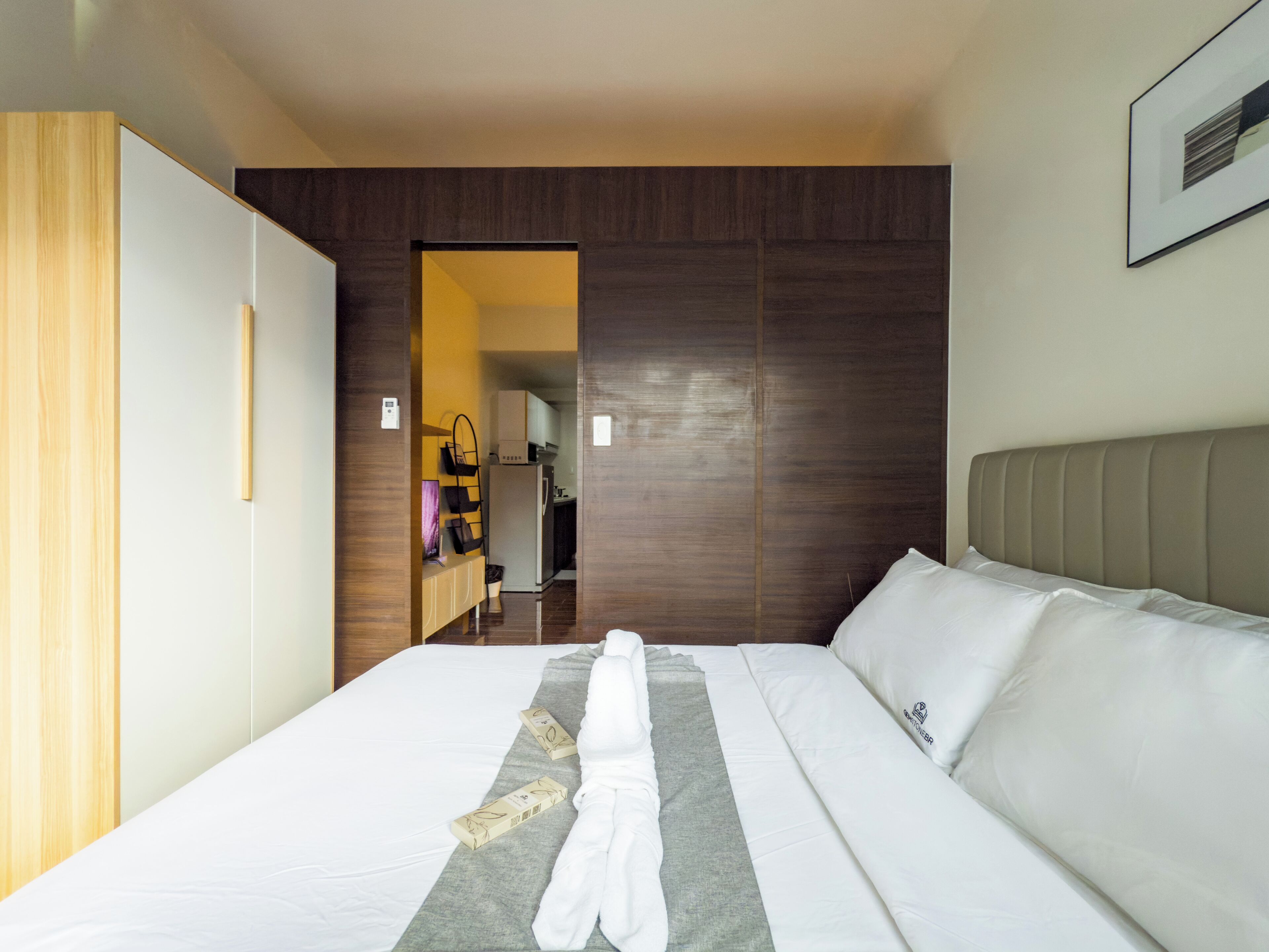 A hotel room with a large bed, a wooden wardrobe, a bathroom, and a kitchenette.