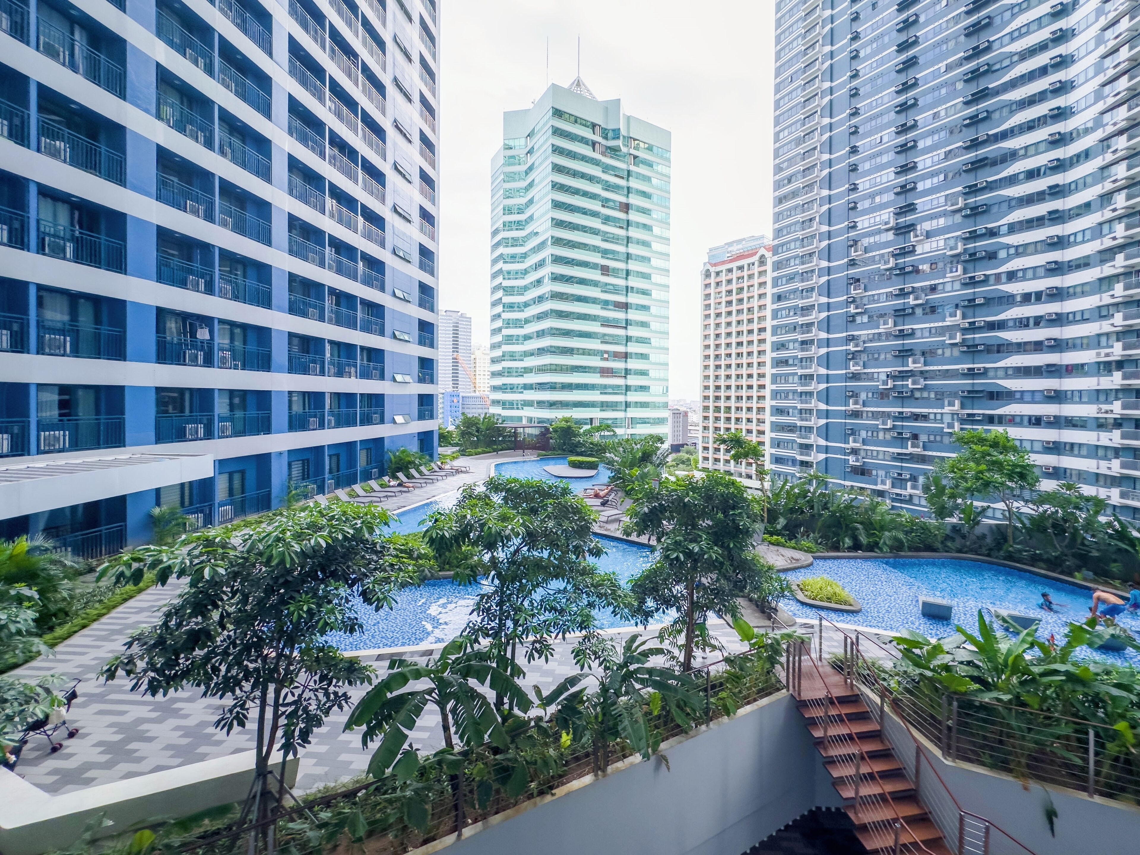 A modern residential complex with multiple high-rise buildings, a central swimming pool, and surrounding greenery.