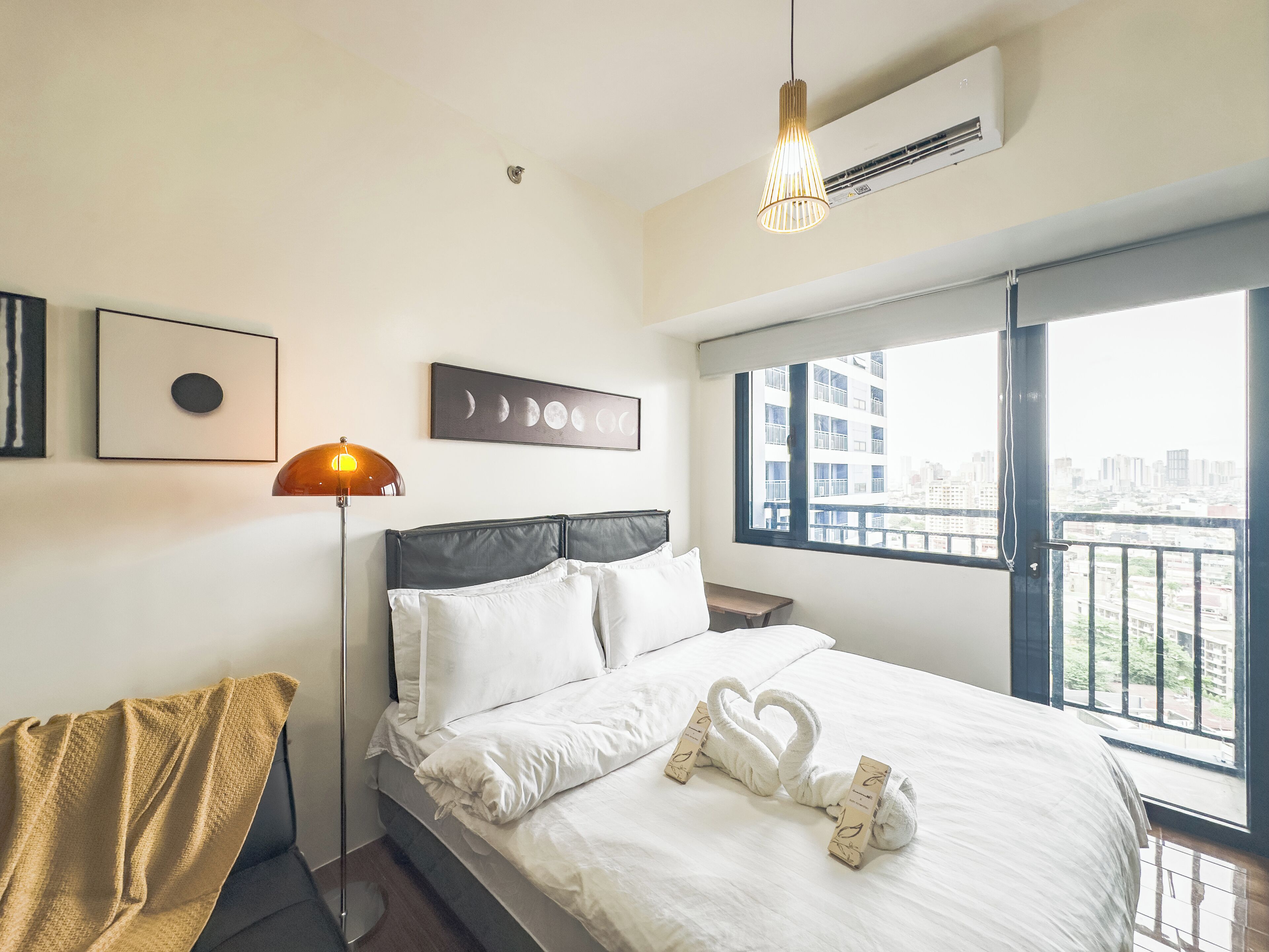 Quarto de hotel com cama, luminária de cabeceira, ar condicionado na parede e janela com vista para a cidade.