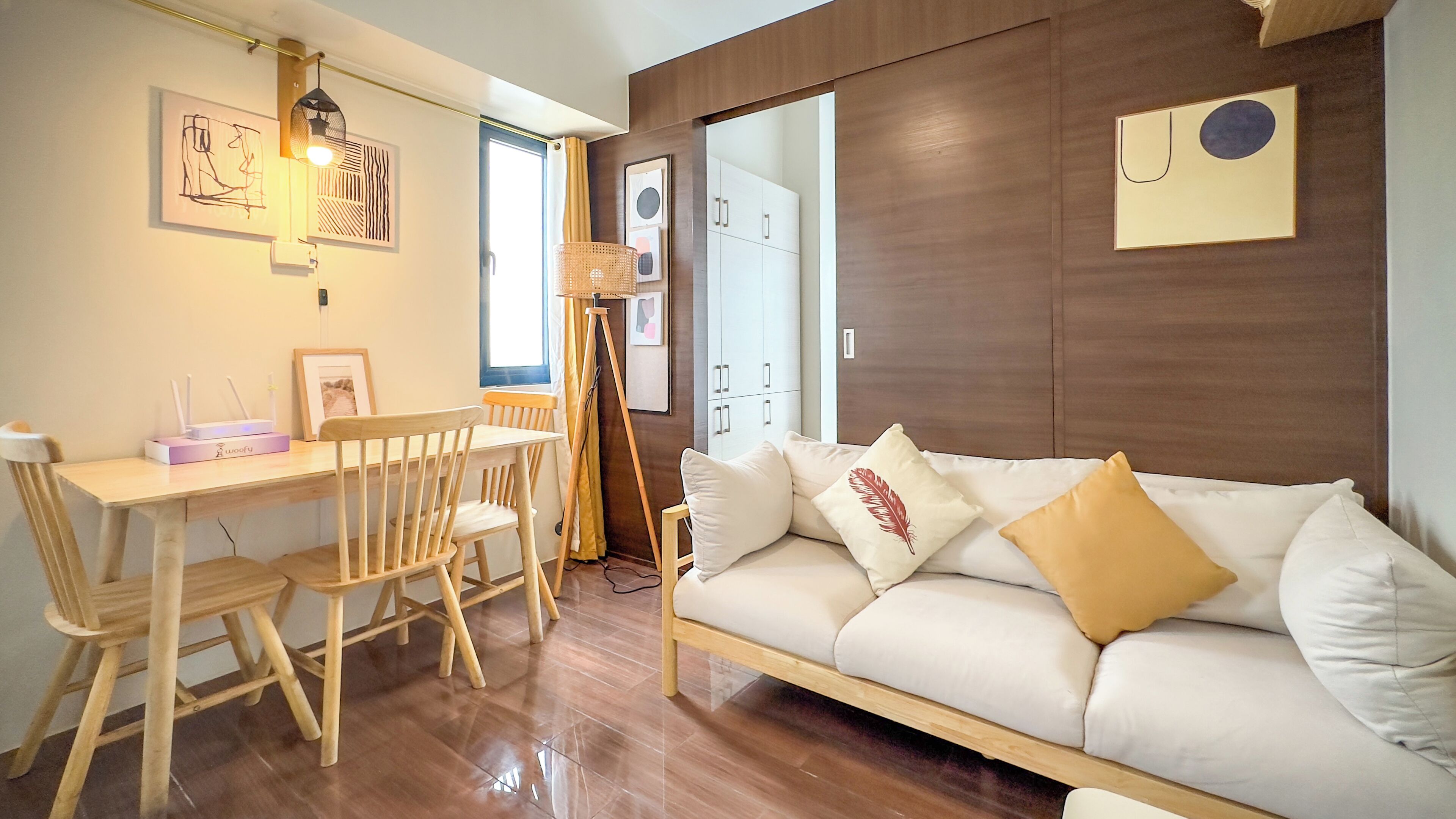 Un salon moderne avec un plancher en bois, un canapé blanc agrémenté de coussins décoratifs, une table à manger en bois avec des chaises et un lampadaire.