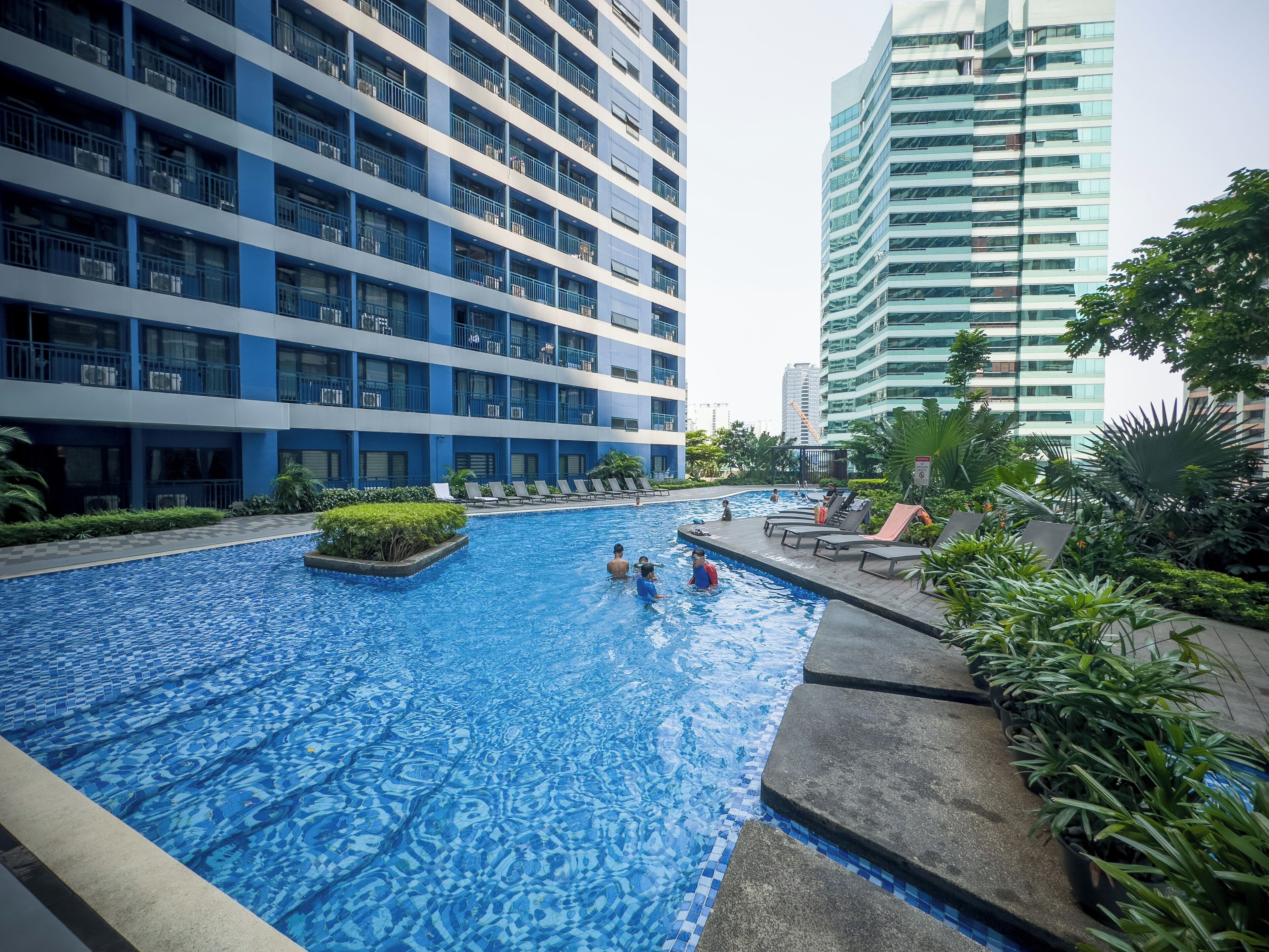 A swimming pool with a tiled pattern, surrounded by lounge chairs and potted plants.