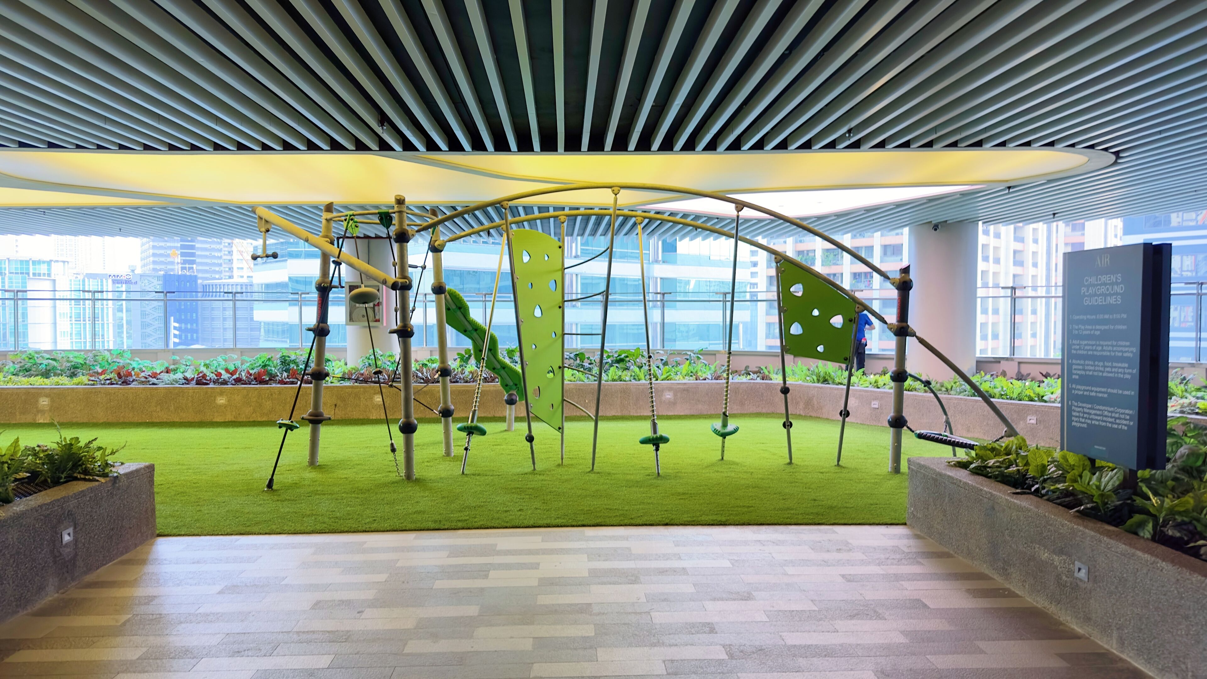 Un espace de jeux intérieur doté de structures d’escalade et d’un revêtement d’herbe artificielle, le tout se fondant dans un décor représentant un paysage urbain.