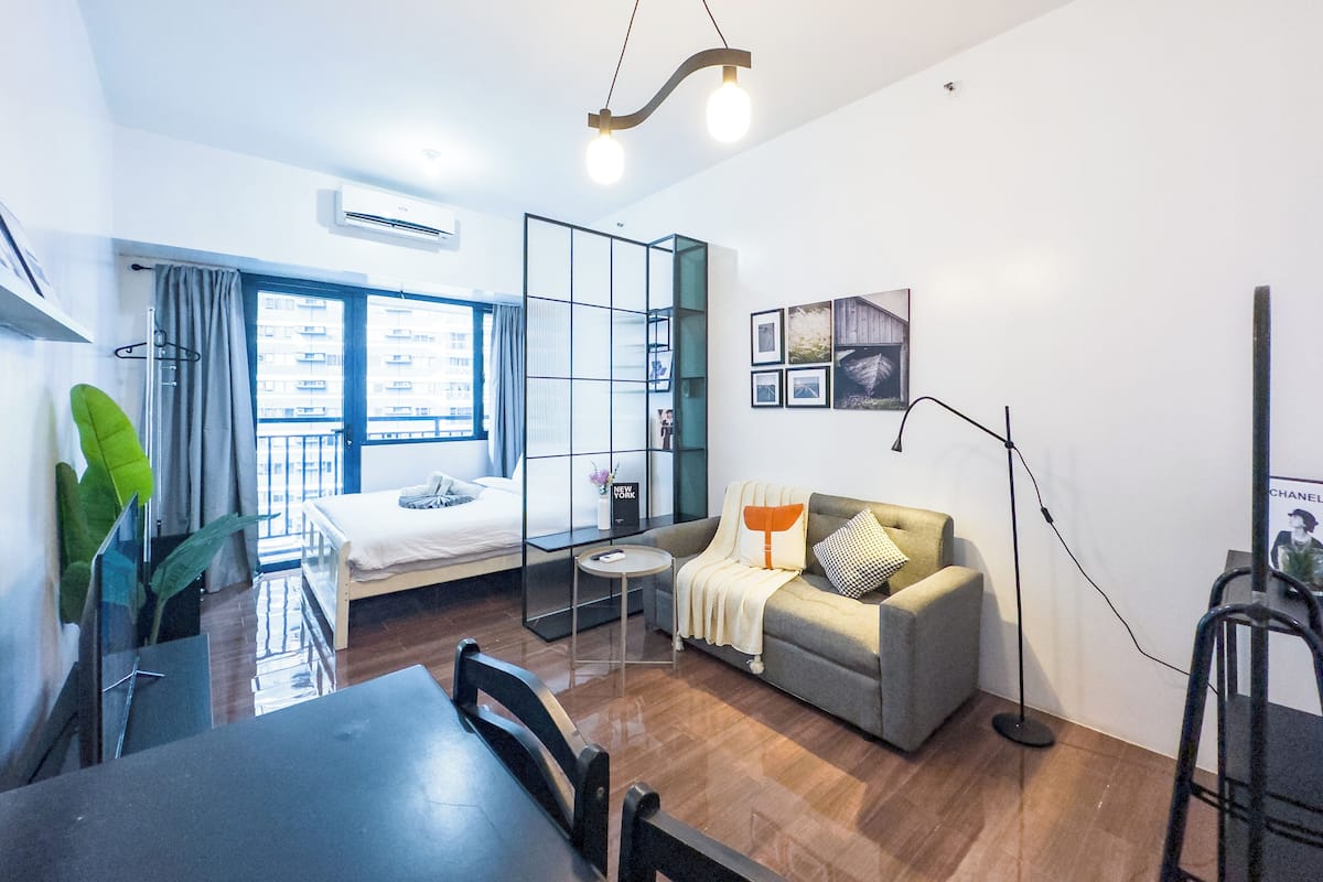 A modern apartment with a balcony, a sofa, a dining table, and a large window.