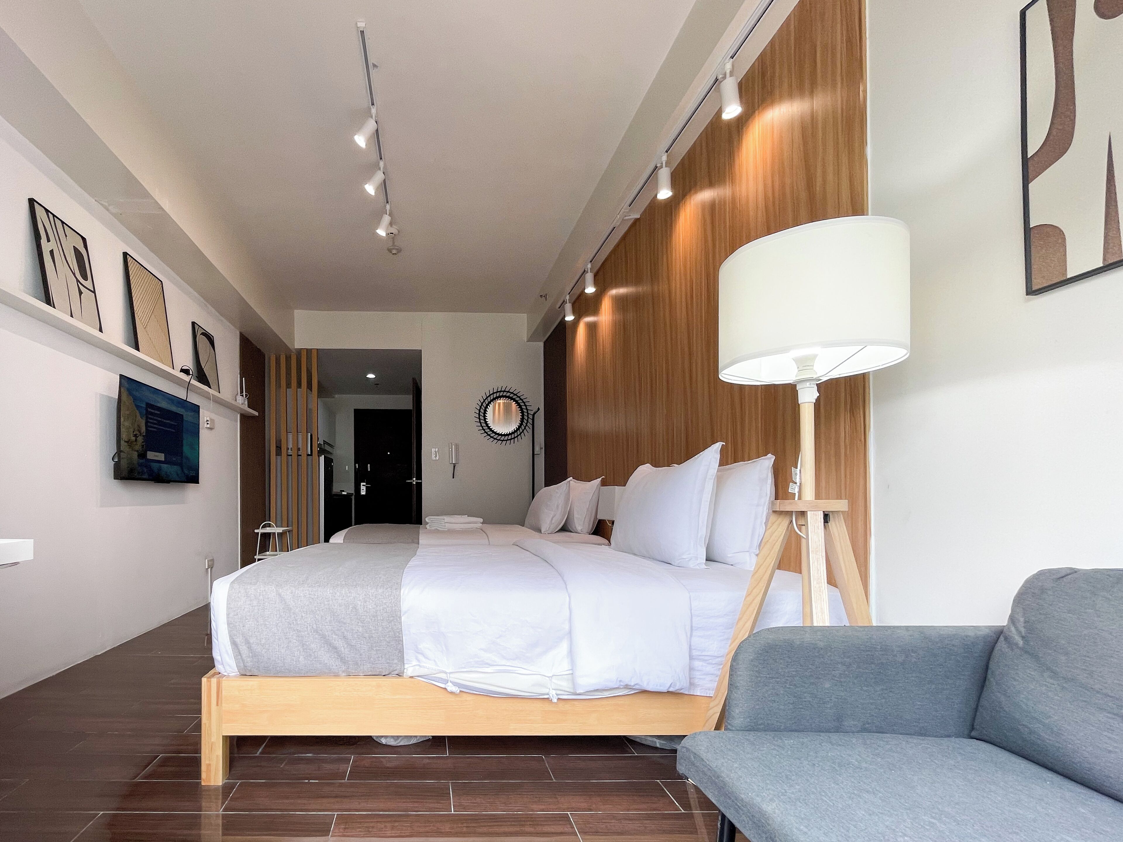 A modern hotel room with a large bed, a grey sofa, and a wall-mounted lamp.
