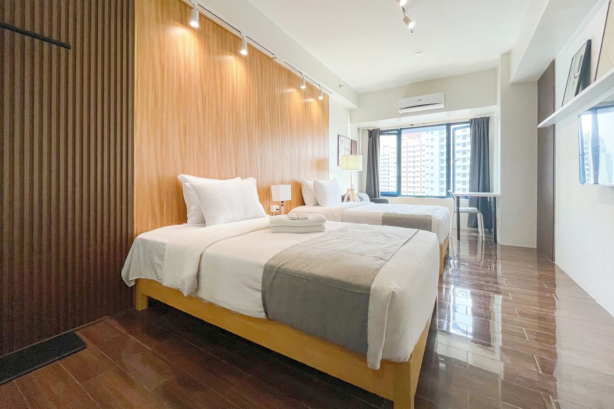 A modern hotel room with a large bed, a desk, and a view of the city through the window.