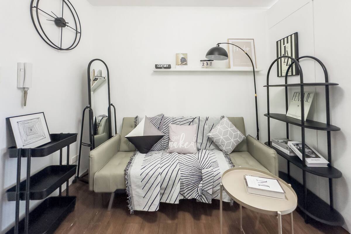 A modern living room with a sofa, a coffee table, a side table, a bookshelf, a wall clock, and a mirror.