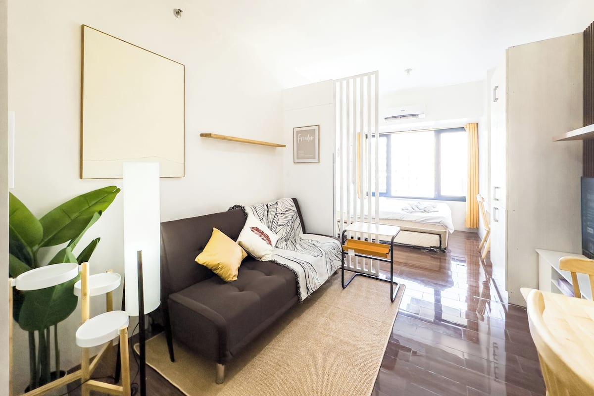 A modern, well-lit room with a dark brown sofa, a small wooden table, and a bed with a white headboard.