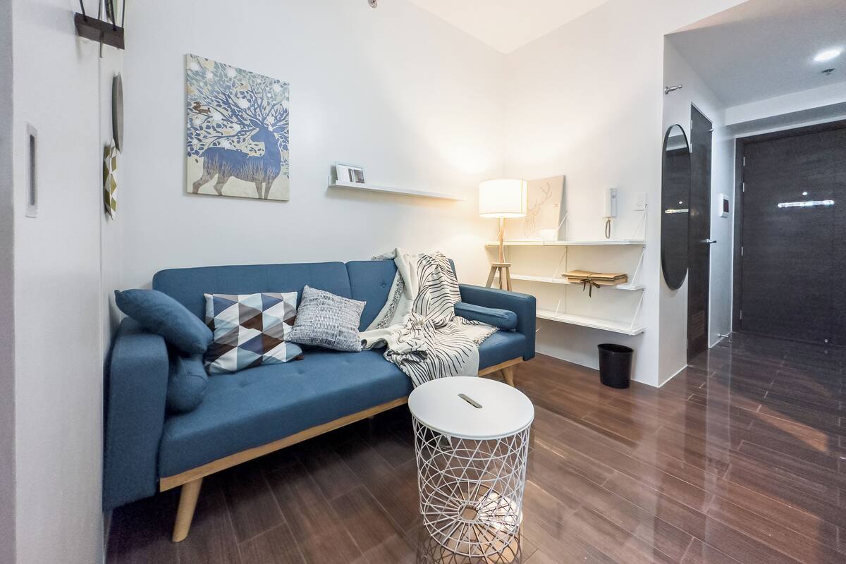 A modern living room with a blue sofa, a small white side table, and a wooden floor.