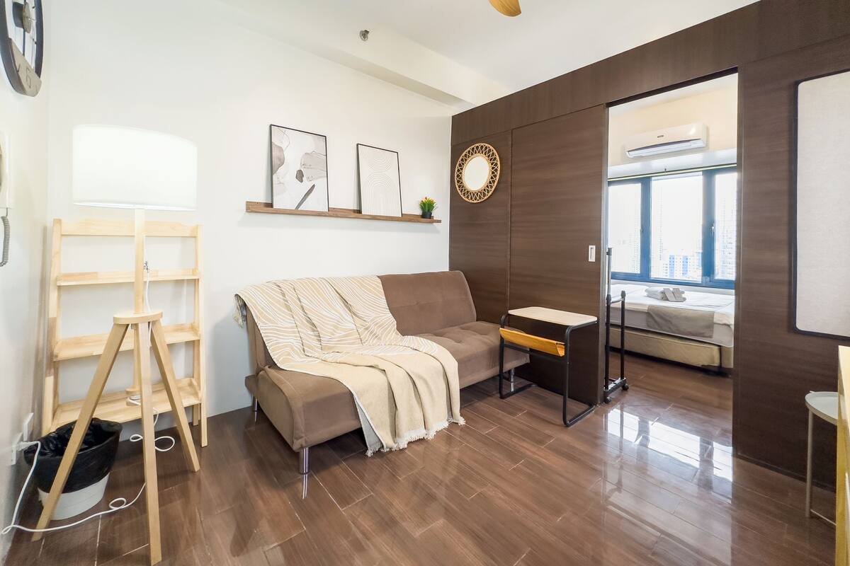 A modern living room with a wooden floor, a sofa, a desk, and a ceiling fan.