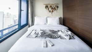 A hotel room with a large window, a bed with white bedding, a remote control, and a wall decoration. - GemstoneBR II in SMDC Air Residences (Makati)