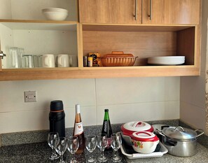 Una cucina con mobili in legno, un piano di lavoro in granito e diversi utensili da cucina, tra cui bicchieri da vino, bottiglie e pentole.
