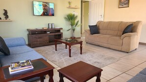 A living room with a sofa, a coffee table, a TV, and a door leading to another room.