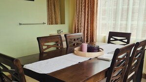A dining area with a wooden table, four chairs, a mirror, a window with curtains, and a framed picture on the wall.