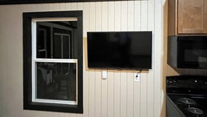 Eine Küche mit einem schwarzen Herd, einem schwarzen Backofen, einem an der Wand befestigten Fernseher und einem Fenster mit weißem Rahmen.