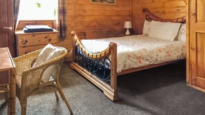 Una habitación de madera con una cama, una silla, un escritorio y un cuadro en la pared.