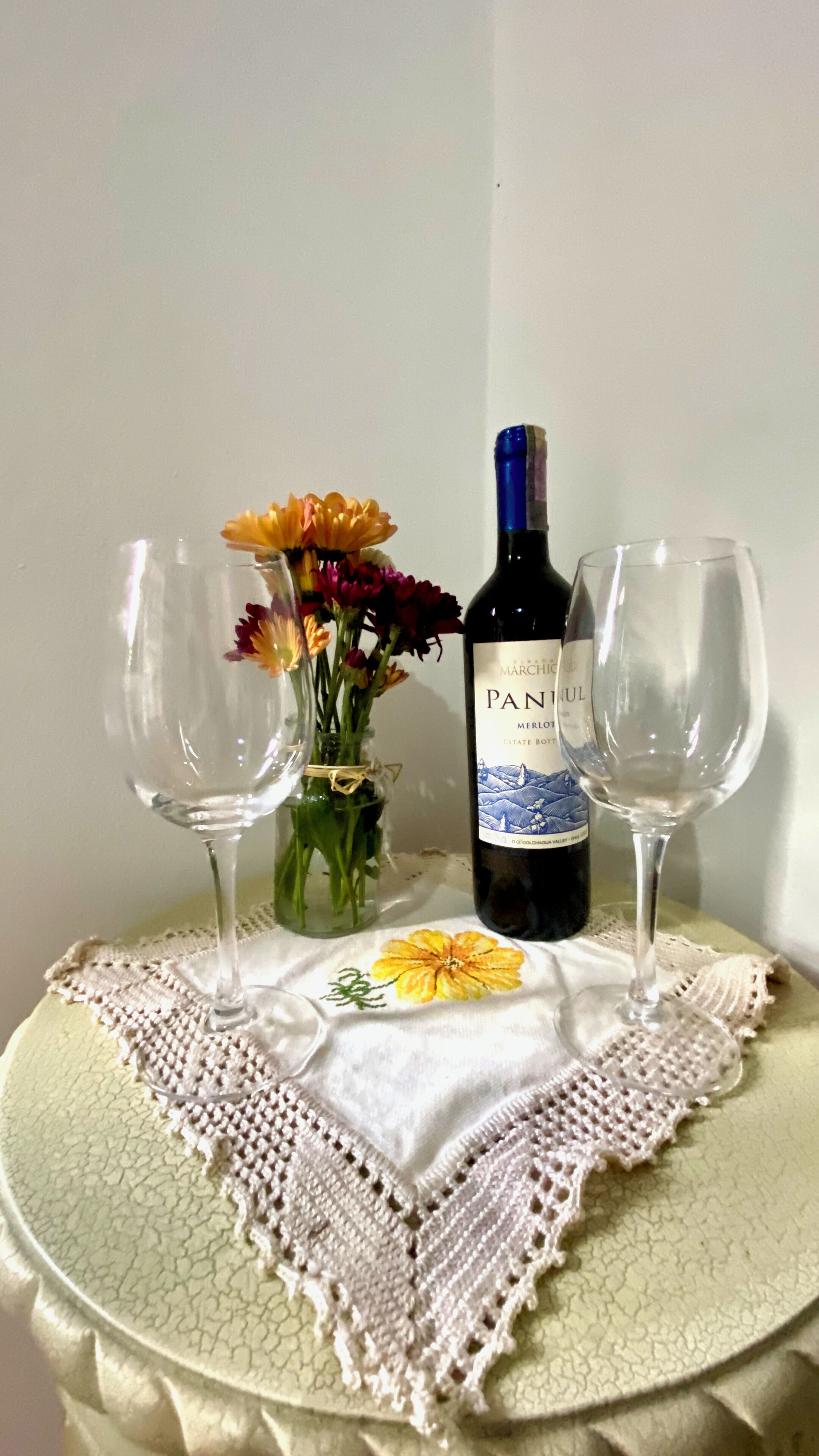 Una mesa con una botella de vino, dos copas y un florero.