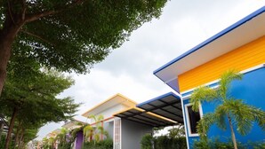 A row of modern buildings with a covered walkway, surrounded by greenery and trees. - OYO 75487 Prang Thip 306 Resort (Bangkok)