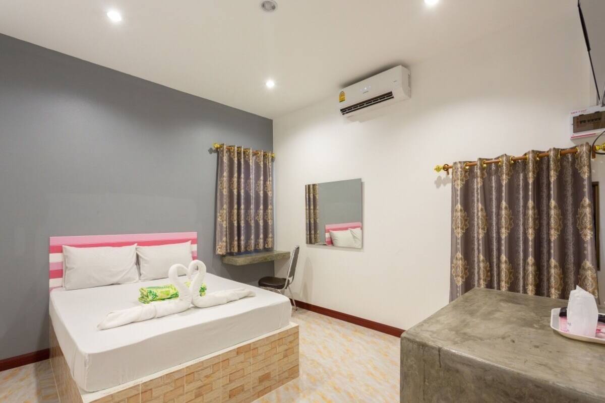 A hotel room with a bed, a desk, a chair, an air conditioner, and a bathroom.