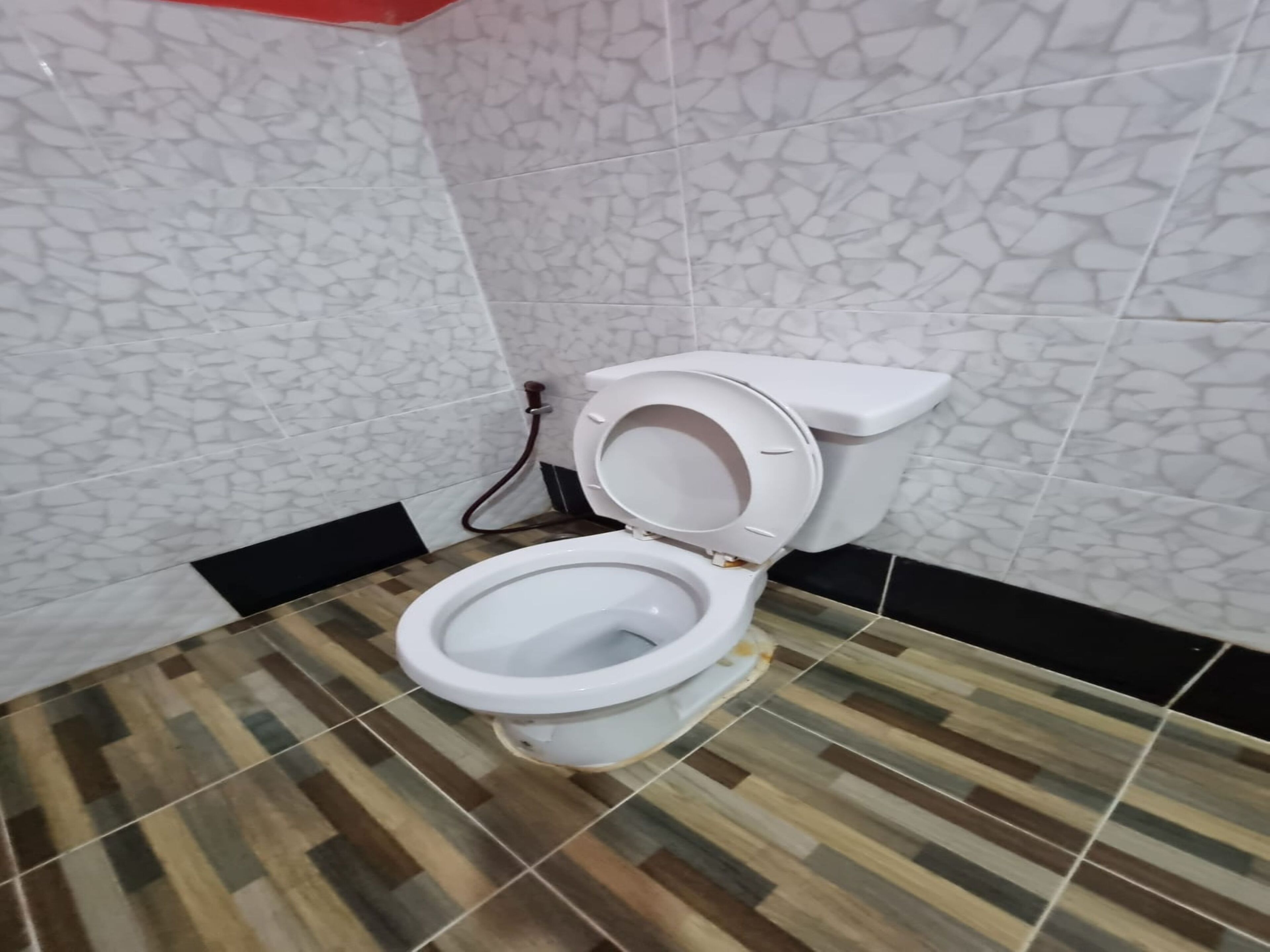 A bathroom with a white toilet, patterned floor tiles, and white walls with a stone-like texture.