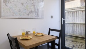 Una mesa de comedor con dos platos de croissants y vasos de jugo de naranja, un mapa en la pared y vista a una cerca de madera a través de una puerta de vidrio.