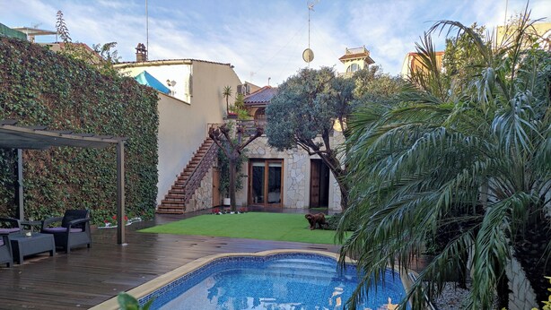 Une piscine dotée d’une terrasse carrelée, entourée d’une végétation luxuriante et d’un escalier en pierre menant à un bâtiment dont le toit est également recouvert de tuiles.
