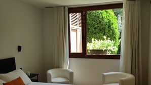 Une chambre à coucher avec un lit, deux chaises, une fenêtre donnant sur un paysage verdoyant et une table de chevet.