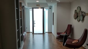 Un intérieur moderne avec un plancher en bois, un coin salon doté de deux fauteuils et une grande porte vitrée donnant sur un espace lumineux.