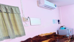 Quarto com um banco de madeira, ar condicionado, geladeira e telefone fixo na parede.