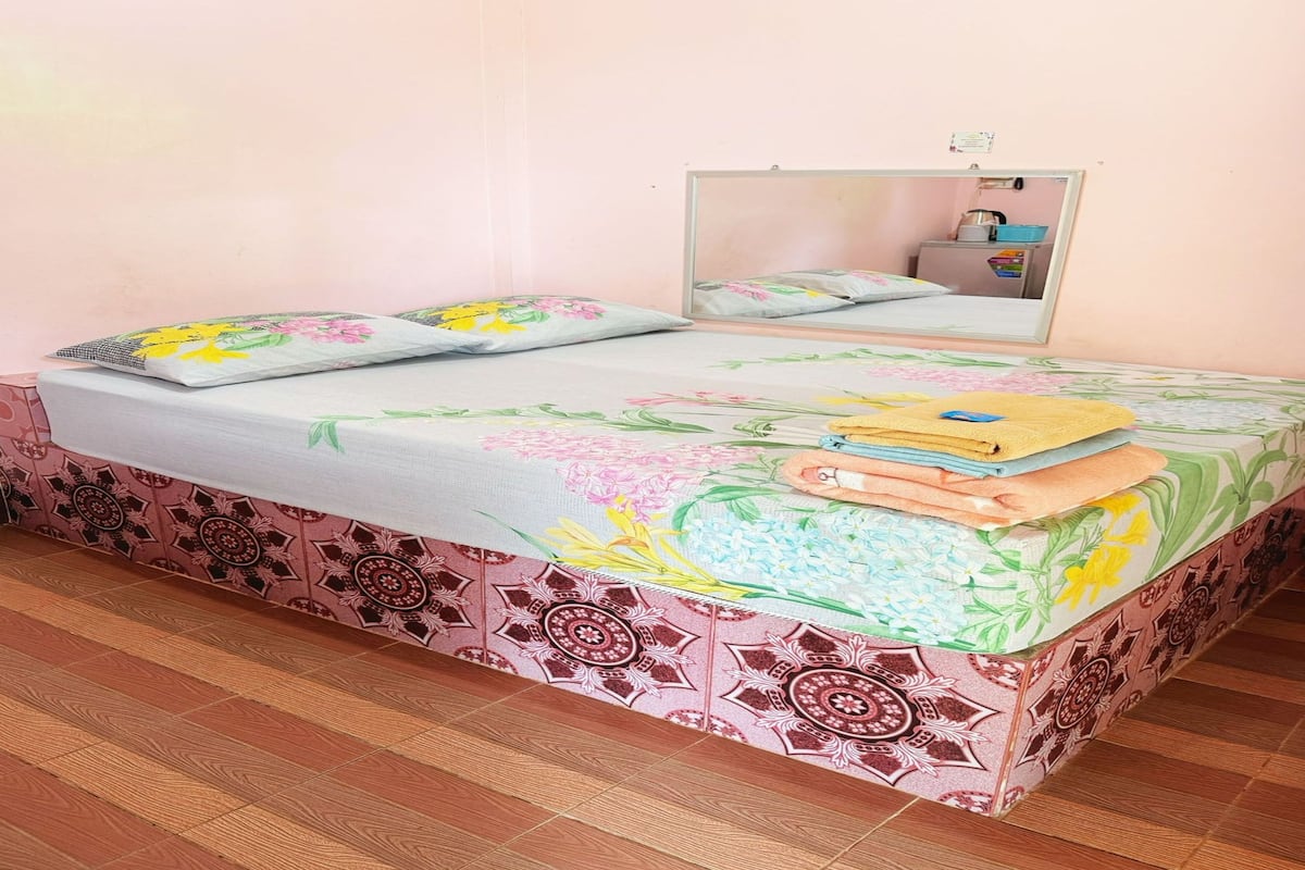 A bed with floral bedding, a mirror, and a stack of towels.