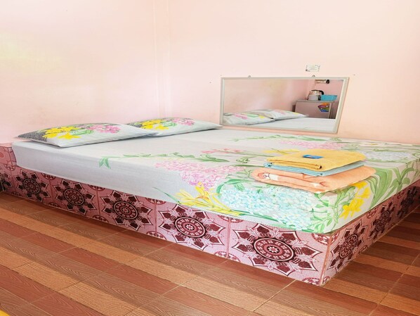 Una cama con ropa de cama floral, un espejo y una pila de toallas.