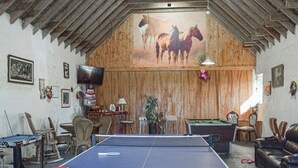 Ein Raum mit Tischtennisplatte, Billardtisch und einer Holzbalkendecke mit einem Wandgemälde von Pferden.