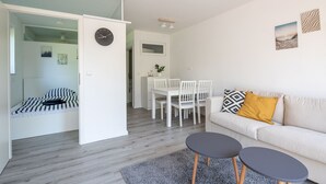Una sala moderna con un sofá, dos mesitas, un comedor con sillas y un reloj en la pared.