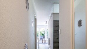 Un pasillo con suelo de madera, paredes blancas y una puerta que da a un balcón.