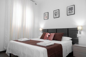 Una cama bien hecha con ropa de cama blanca y marrón, un cabecero con listones horizontales y tres cuadros en la pared arriba.