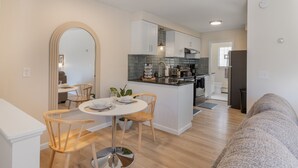 Een moderne keuken met witte kasten, een centraal eiland en een eethoek met houten stoelen en een witte tafel.