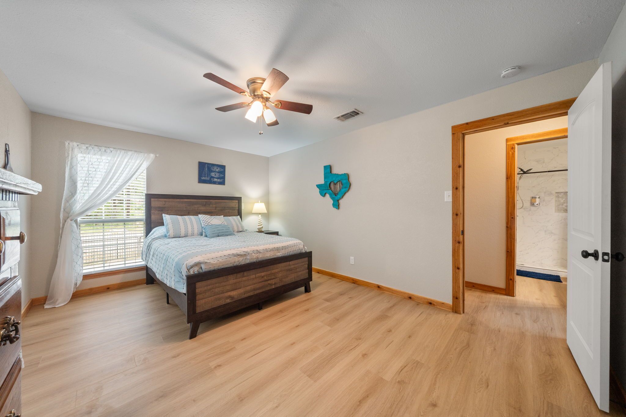 A bedroom with a wooden bed, a ceiling fan, a window with curtains, and a door leading to another room.