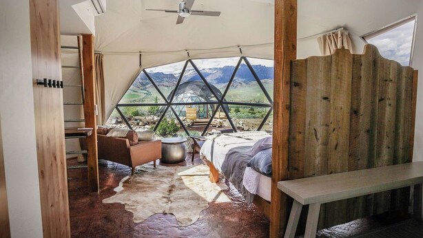 Een tent met een bed, een stoel, een tafel en uitzicht op bergen.