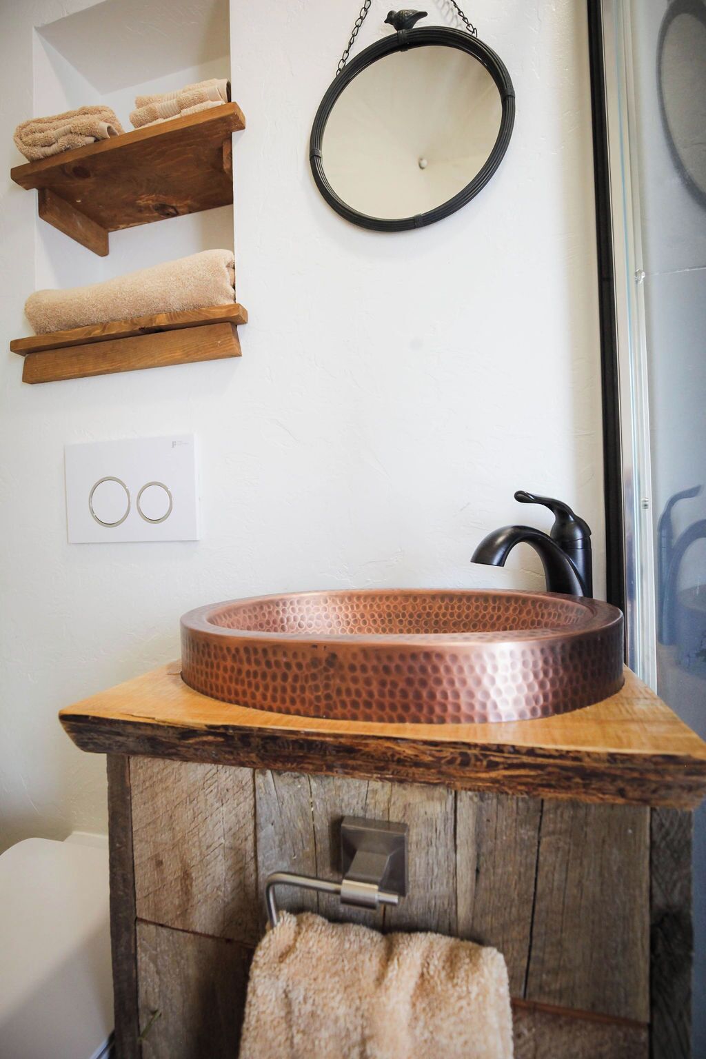 Un baño con lavamanos de cobre, estantes de madera, un espejo colgado y un perchero.
