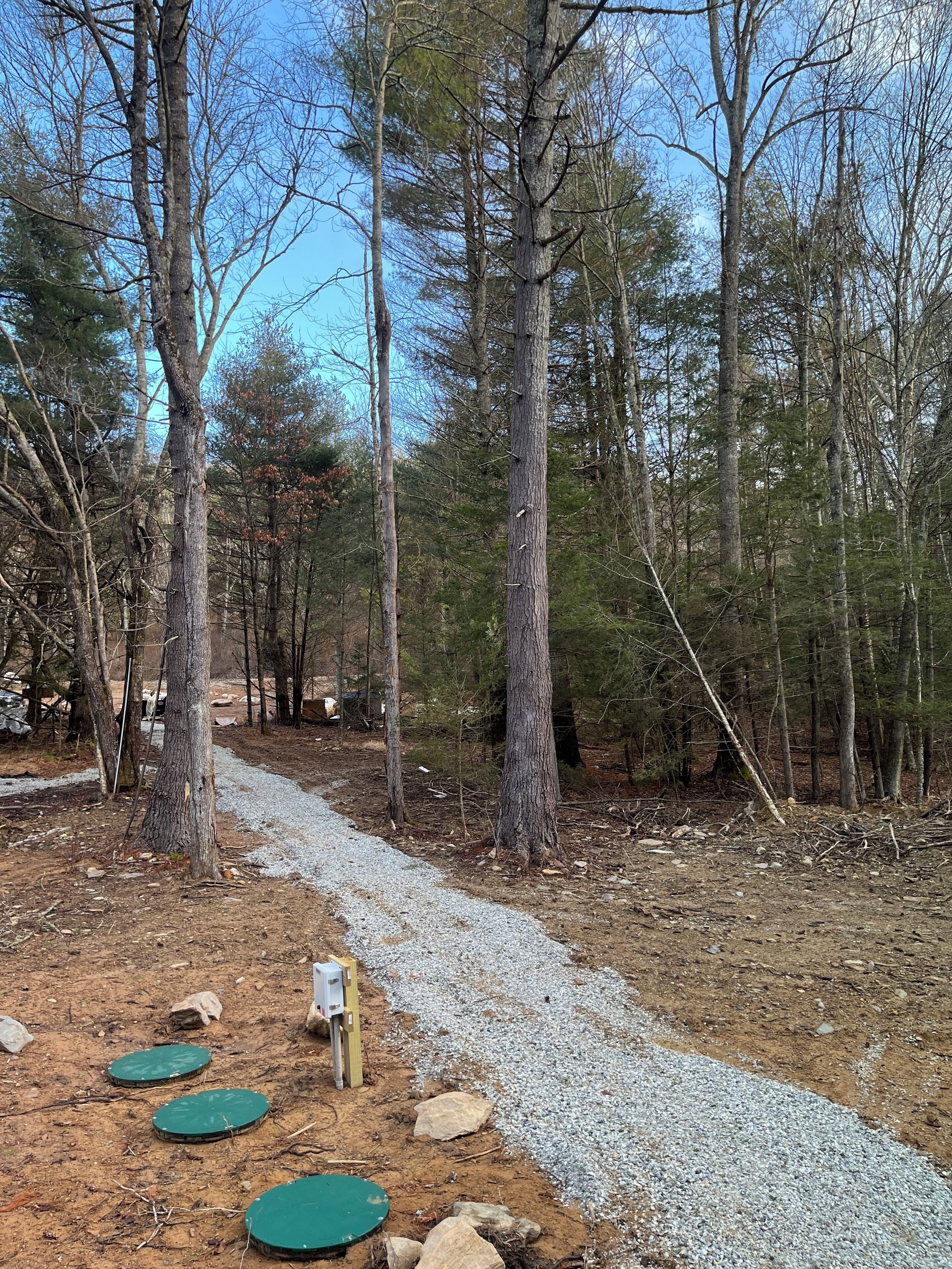 A forested area with a gravel path, wooden structures, and green circular covers on the ground.
