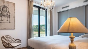 Une chambre dotée d’un grand lit, d’un fauteuil moderne, d’un lustre et offrant une vue sur l’extérieur.