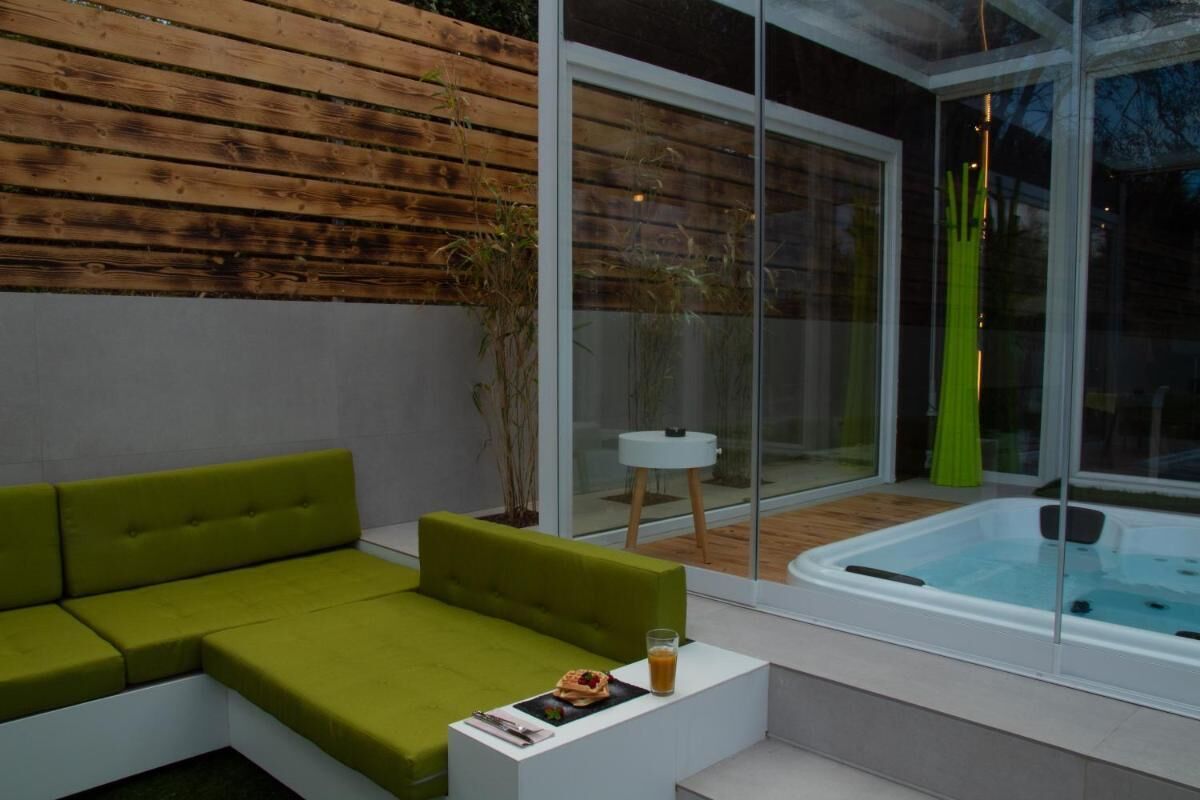 Un espace de détente extérieur moderne, avec un canapé vert, une petite table sur laquelle est posée une boisson et un jacuzzi.
